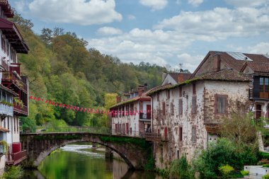 Saint Jean Pied de Port, Fransa 'da bir nehir boyunca uzanır. Köprü kırmızı bayraklarla süslenmiş ve kasaba ağaçlarla çevrili.
