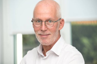 Gözlüklü ve beyaz gömlekli bir adam gülümsüyor. Beyaz bir gömlek ve gözlük takıyor.