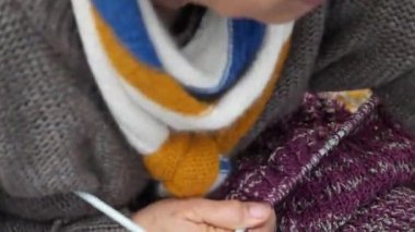 Bir kişi çizgili mor bir kazak örüyor. Süveter üzerinde çalışmak için örgü iğnesi kullanıyor.