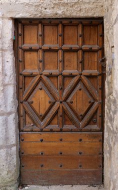 Taş çerçeveli ahşap bir kapı ve arkasında da taş bir duvar. Kapının üzerinde elmas desenli ve küçük deliklerle kaplı.