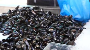 Balıkçı bir yığın midyeyi ayırır. Yığın büyüktür ve birçok midye içerir..