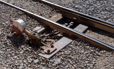 Yerde kırmızı-beyaz işareti olan bir tren yolu. Sinyalin bir sürgüsü eksik.