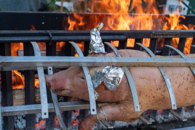 Izgarada üzerinde folyo olan bir domuz pişiriliyor. Izgara yanıyor ve domuz alevlerle çevrili.