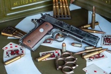 Silah bir deste kurşun ve bir deste iskambil kağıdıyla bir masanın üzerinde duruyor. Olay yeri kaotik ve tehlikeli. Silah ve kurşunlar şiddet içeriyor.