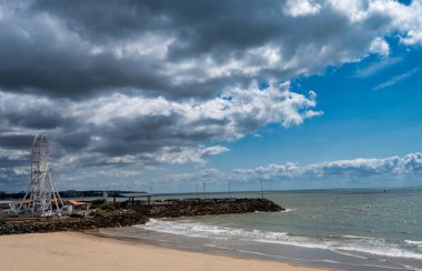 Sahilde büyük bir dönme dolap var. Gökyüzü bulutlu ve su sakin.