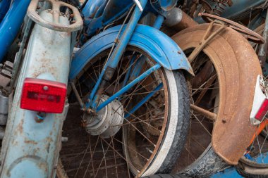 Bir tanesinde kırmızı stop lambası olan eski bir motosiklet yığını. Bisikletler üst üste dizilmiş.