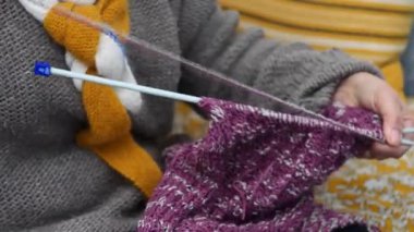 Kadın mor bir kazak örüyor.