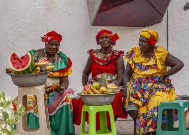 PALENQUERA, CARTAGENA, COLOMBIA, 20 Şubat 2024: Eski Cartagena kasabasındaki neşeli taze meyve sokak satıcısı namı diğer Palenquera. Geleneksel giyinmiş mutlu Afro-Kolombiyalı kadın, Kolombiya kültürü.