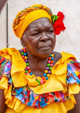 PALENQUERA, CARTAGENA, COLOMBIA, 20 Şubat 2024: Eski Cartagena kasabasındaki neşeli taze meyve sokak satıcısı namı diğer Palenquera. Geleneksel giyinmiş mutlu Afro-Kolombiyalı kadın, Kolombiya kültürü.