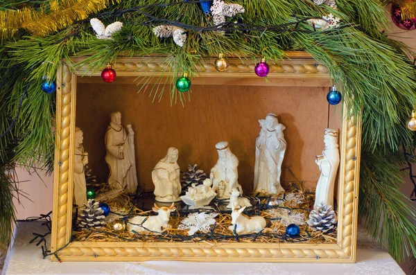 Christmas festive nativity scene made of plywood with white ceramic figures under the Christmas tree.