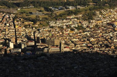 Cruz Loma 'dan çekilen Quito, Ekvador şehrinin çarpıcı hava manzarası, evleriyle, binalarıyla ve Ulusal Yeminin önde gelen bazilikasıyla kentsel yayılmayı gösteriyor. Akşam ışığı aydınlanmışlar arasında çarpıcı bir zıtlık yaratır. 