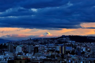 And Dağları 'nın ihtişamının takdir edilebileceği Quito şehrinin, bulutlar tarafından çerçevelenmiş Cotopaxi volkanı ve şehrin ufuk çizgisi ile günbatımında ilginç bir panoramik manzarası..