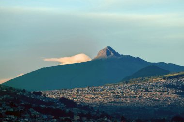 Quito, Ekvador 'un güney kesiminin panoramik görüntüsü, bir And vadisinde altın saat boyunca yer almaktadır. Yükselen güneş şehrin binalarını aydınlatırken, görkemli Corazon yanardağı açık bir gökyüzünün altında yükseliyor..
