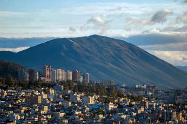 Kuzey Quito 'nun panoramik manzarası, arka planda Casitahua yanardağının heybetli varlığı ile çerçevelenmiş binaları ve evleri ile şehrin kentsel genişlemesini gösteriyor..