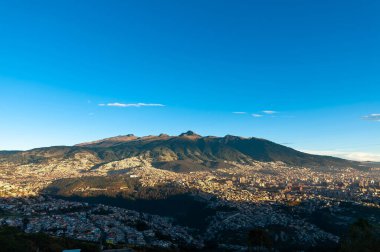 Ekvador 'un başkenti Quito' nun muhteşem panoramik manzarası, altın bir gündoğumunda. Güneş, görkemli Pichincha yanardağının yamaçlarını aydınlatır. Ve büyük And şehri manzarasını..