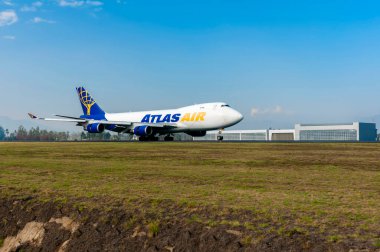 Bir Atlas Air Boeing 747 kargo uçağı indikten sonra pistte yüksek hızda ilerliyor. Sahne masmavi bir gökyüzünün altında.