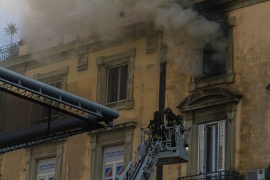 Napoli, İtalya - 15 Şubat 2023 - Pencereden duman yükselen ev yangını. Garibaldi Meydanı, Napoli, İtalya. Magirus İtfaiye sepetinde veya kafesinde ateşin yanında iki itfaiyeci vardı.