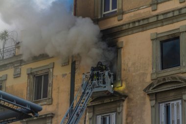 Napoli, İtalya - 15 Şubat 2023 - Pencereden duman yükselen ev yangını. Garibaldi Meydanı, Napoli, İtalya. Magirus İtfaiye sepetinde veya kafesinde iki itfaiyeci solunum cihazıyla, manzara.