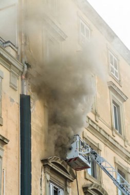Napoli, İtalya - 15 Şubat 2023 - Pencereden duman yükselen ev yangını. Garibaldi Meydanı, Napoli, İtalya. İtfaiye sepetinde ya da kafesinde solunum cihazında iki itfaiyeci vardı..