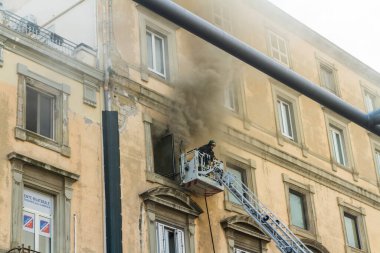 Napoli, İtalya - 15 Şubat 2023 - Pencereden duman yükselen ev yangını. Garibaldi Meydanı, Napoli, İtalya. İtfaiye sepetinde veya kafeste tek bir itfaiyeci, manzara.
