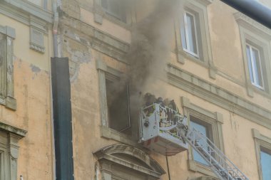 Napoli, İtalya - 15 Şubat 2023 - Pencereden duman yükselen ev yangını. Garibaldi Meydanı, Napoli, İtalya. İtfaiye sepetine veya kafese iki itfaiyeci, biri girmeye hazırlanıyor..
