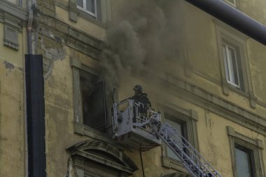 Napoli, İtalya - 15 Şubat 2023 - Pencereden duman yükselen ev yangını. Garibaldi Meydanı, Napoli, İtalya. İtfaiye sepetinde veya kafeste tek bir itfaiyeci, peyzaj, telefon....