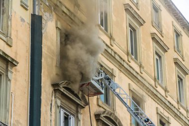 Napoli, İtalya - 15 Şubat 2023 - Pencereden duman yükselen ev yangını. Garibaldi Meydanı, Napoli, İtalya. İtfaiye sepetinde ya da kafesinde iki itfaiyeci solunum cihazıyla, manzara....