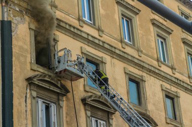 Napoli, İtalya - 15 Şubat 2023 - Pencereden duman yükselen ev yangını. Garibaldi Meydanı, Napoli, İtalya. Magirus İtfaiye sepetinde ya da kafesinde itfaiyeci merdivene tırmanıyor..