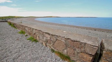 Anglesey, Galler 'in kuzey kıyısında Cemlyn Körfezi. Duvarın kıvrımı, çakıl taşı plajı ve deniz, mavi gökyüzü..