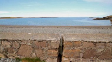 Anglesey, Galler 'in kuzey kıyısında Cemlyn Körfezi. Duvar, çakıl taşı plaj ve deniz, mavi gökyüzü.