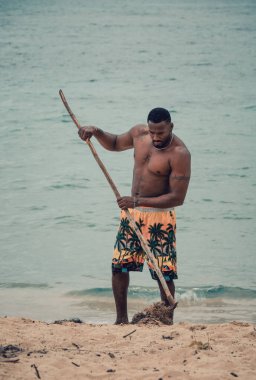 Samana, Dominican Republic, 26 august, 2022. Young and fit Dominican man cleaning the beach with a rake in beautiful and secluded Playa Ermitano.