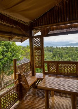 Asya 'daki bir adada, verandadan ya da bambudan yapılmış bir bungalovun verandasındaki palmiye ağaçlarından oluşan bir orman manzarası. Eko pansiyon ya da tatil havası, tropikal tatiller.