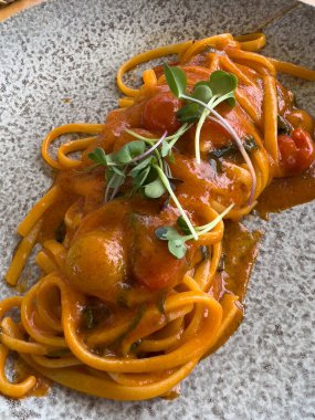 Basit ve lezzetli bir restoran tabağının üstünden yakın çekim: taze domates soslu makarna ve fesleğen, bitkisel dekorasyonlu.