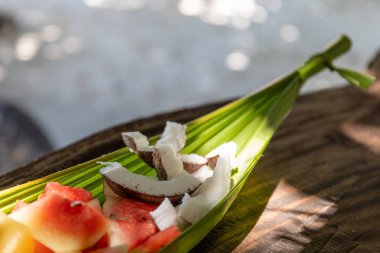 Bir tabak tropikal meyve, karpuz, hindistan cevizi, mango ve ananas yakın çekim, egzotik bir sahilde bir muz yaprağında servis edilir..