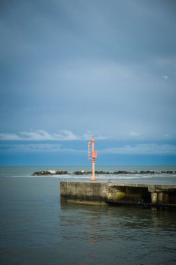 Port and pier equipment, little beacon on the pier in a Riviera Romagnola beach location. dramatic sky in a winter afternoon. Winter sea. Moody and gloomy day. clipart