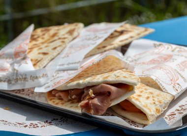 İki Piadina Romagnola markasız ama yağlı kağıda sarılmış, İtalya 'nın Riviera Romagnola bölgesinden özgün sokak yemekleri üst üste istiflenmiş. Prosciutto Crudo jambonu. 