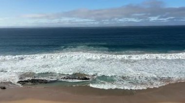 Aşağıdaki sahildeki kayalıkların üzerinden, güneşli bir günde, devasa, güçlü ve köpüklü dalgalarla manzarayı seyret. Doğanın inanılmaz gücü. Yatay video. Escalera Sahili, Fuerteventura.