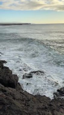 El Cotillo 'nun tepesinden, aşağıdaki kayalıklardan, devasa güçlü deniz köpüklü dalgalar, neredeyse gün batımına yakın. Doğanın inanılmaz gücü. Dikey video.
