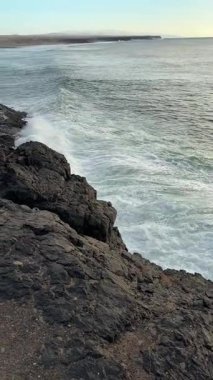 El Cotillo 'nun tepesinden, aşağıdaki kayalıklardan, devasa güçlü deniz köpüklü dalgalar, neredeyse gün batımına yakın. Doğanın inanılmaz gücü. Dikey video.