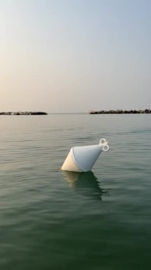 İtalyan Riviera Romagnola 'sında sakin Adriyatik Denizi' nde süzülen beyaz tekne şamandırası. Gün batımı altın saat, sakin, huzurlu ruh hali, neredeyse denizin ortasında alacakaranlık. Dikey video.