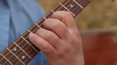 Elleri dışarıda oynayan bir gitaristin ellerinin yakın çekimi. Gitarist dışarıda parkta gitar çalar.