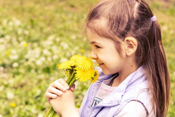 stock image Cute little girl with yellow dandelions on a sunny day on a green nature background. Summer joy - a beautiful girl with yellow dandelions