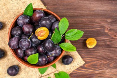 Ahşap bir masada kasede mavi erik. Kesikte erikler var. Üst görünüm, metin için yer. Kopya alanı ile meyve arkaplanı