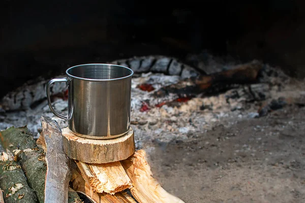 キャンプ用の金属製のマグカップが火のそばに薪の上に立っている キャンプ料理 コピースペース — ストック写真
