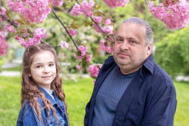 Baba ve kızı parkta çiçek açan saruka 'nın arka planında kameraya bakıp gülümsüyor. Babalar Günü. Kopyalama. Seçici Forcus. Parkta aile tatili. Babalar Günü.