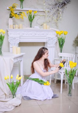 Beyaz elbiseli, uzun dalgalı saçlı güzel bir kız sarı çiçekli bir kitap okuyor..