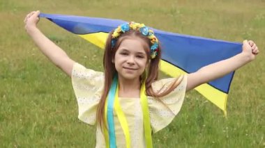 Sarı ve mavi çiçekli bir çelenk içindeki bir kız Ukrayna bayrağını elinde bir tarlanın arka planında tutuyor. Ukrayna Bağımsızlık Bayrak Günü.