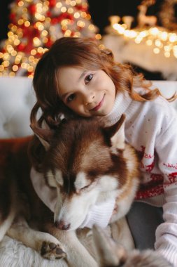 Noel arkaplanında iri kıyım köpeğe sarılan tatlı bir kız..