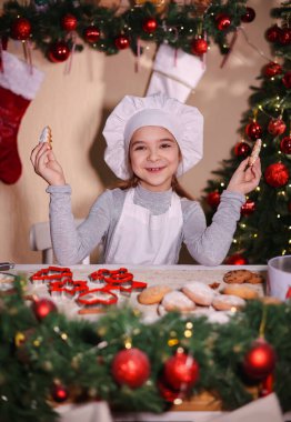 Şefin şapkasıyla neşeli bir kız Noel ağacı şeklinde zencefilli kurabiye gösteriyor.