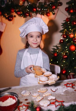 Bir kız Noel arkaplanındaki Noel ağacı şeklinde bir tabakta kurabiye tutuyor. Aile Noel kurabiyesi yapıyor